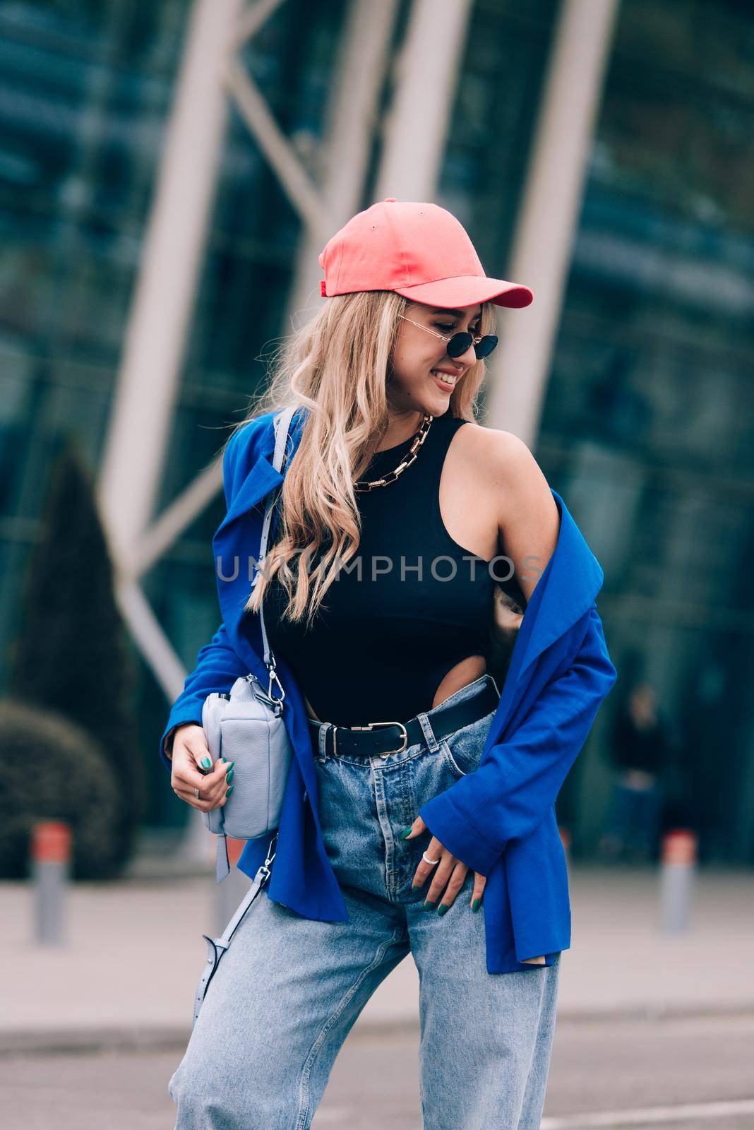 Young sexy blonde hipster woman posing on the street. Wearing blue stylish jacket, jeans and baseball hat and sunglasses. by Ashtray25