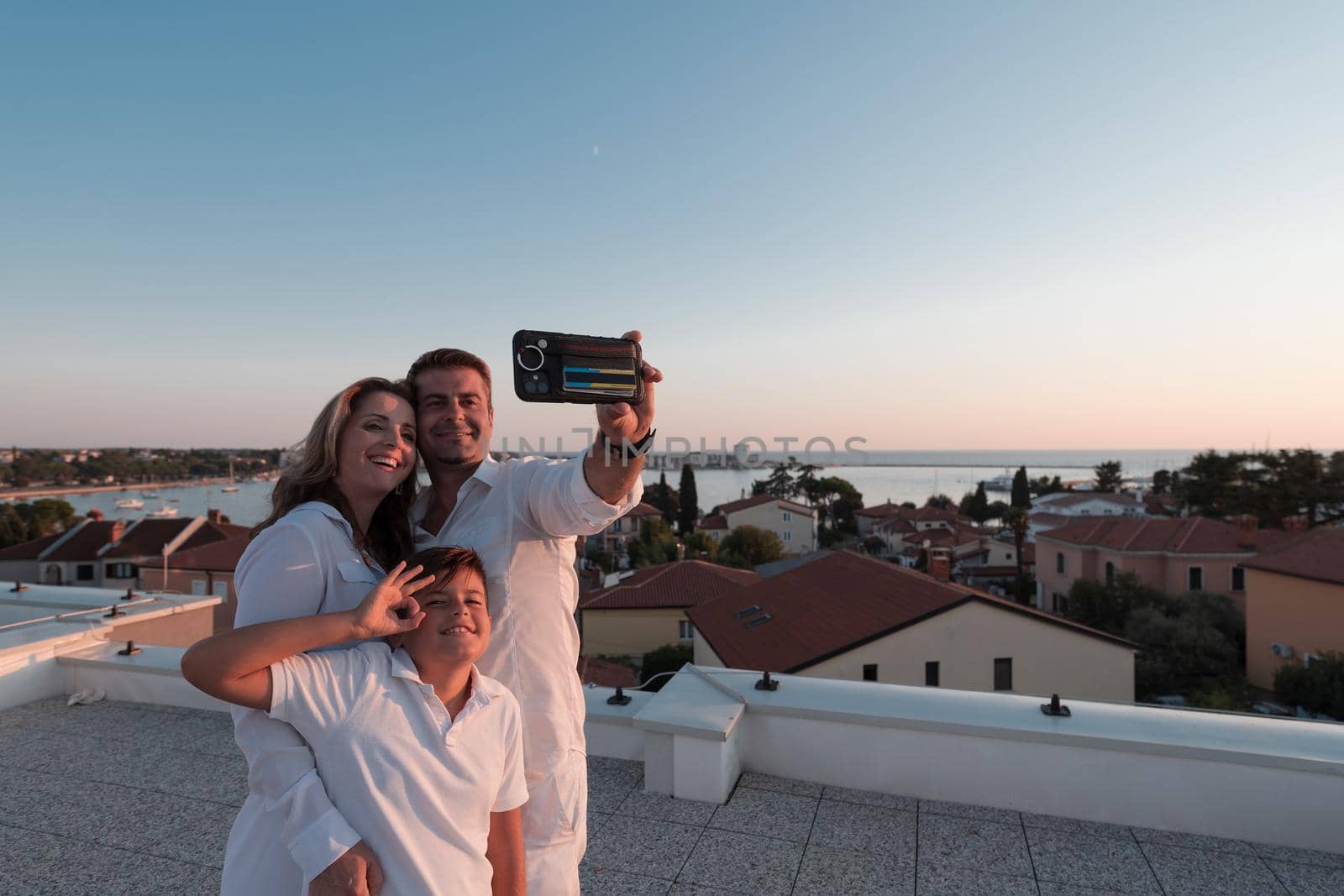 Happy family taking a selfie with a smartphone on the roof of their house at sunset. Selective focus. High-quality photo