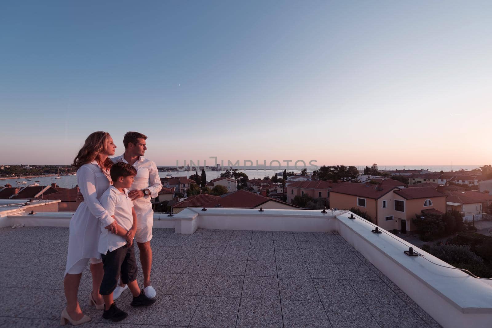 The happy family enjoys and spends time together on the roof of the house while watching the sunset on the open sea together. High-quality photo