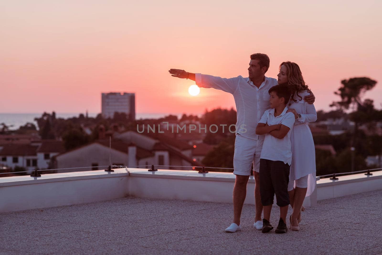 The happy family enjoys and spends time together on the roof of the house while watching the sunset on the open sea together. High-quality photo