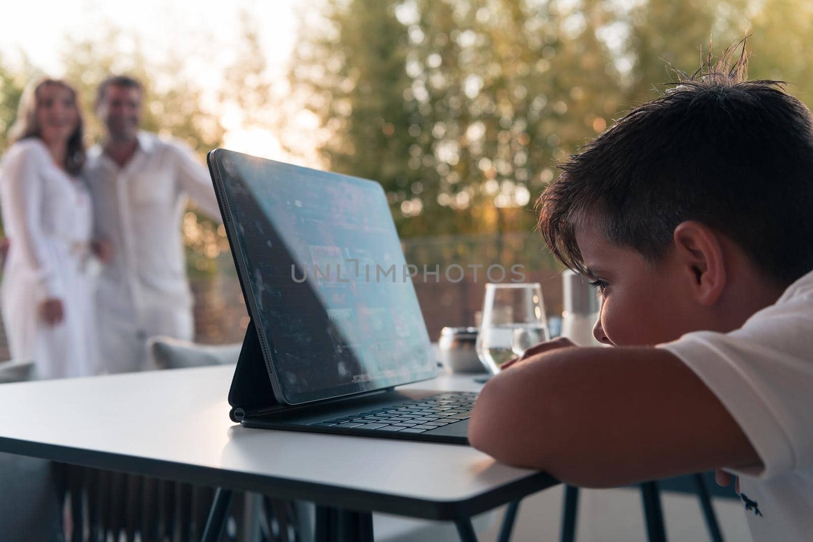 Happy elderly couple resting on the balcony of a luxury house while their son using a tablet. Selective focus. High-quality photo