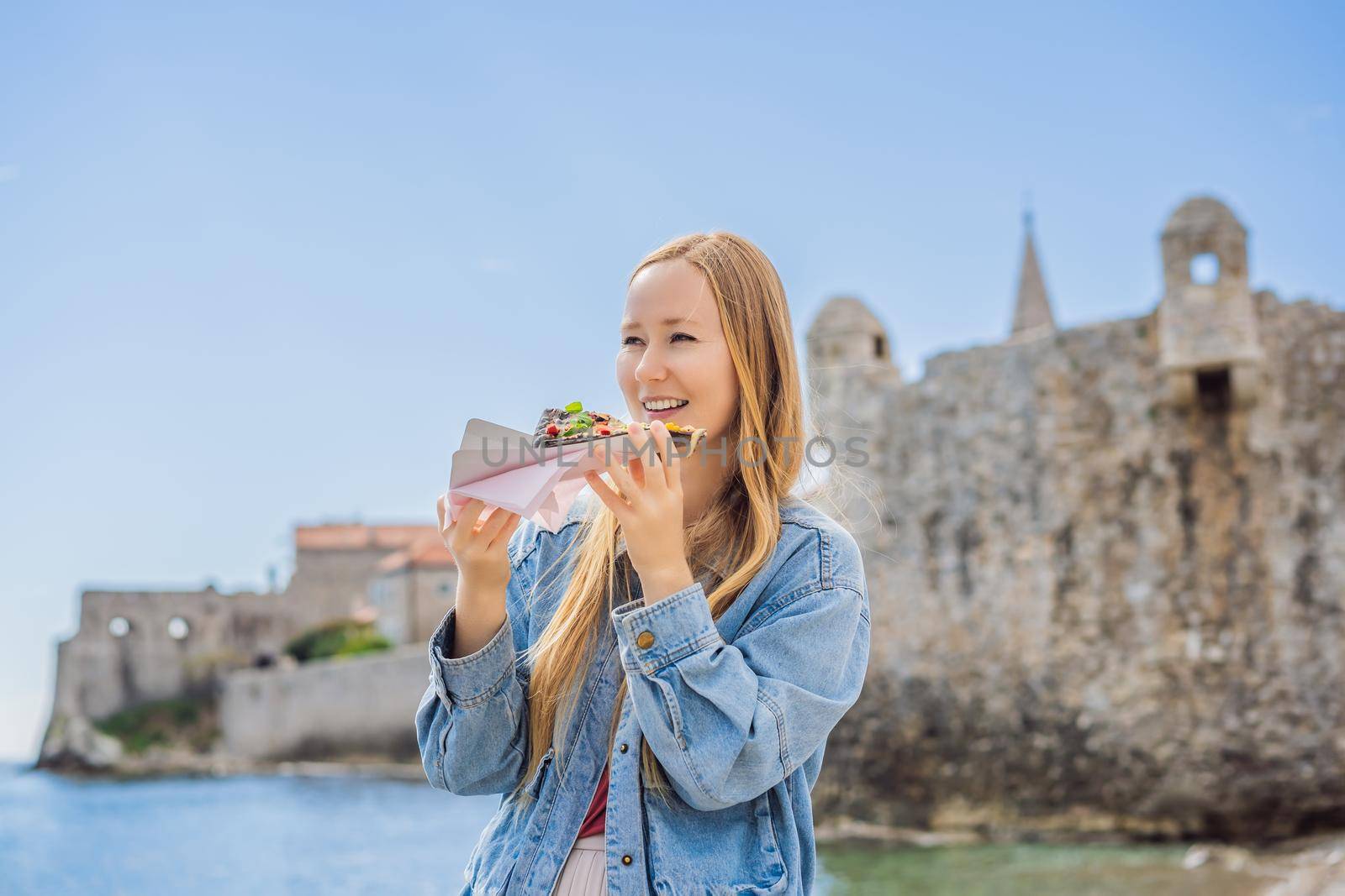 Young woman tourist eating traditional pizza in the old town of Budva. Travel to Montenegro concept by galitskaya