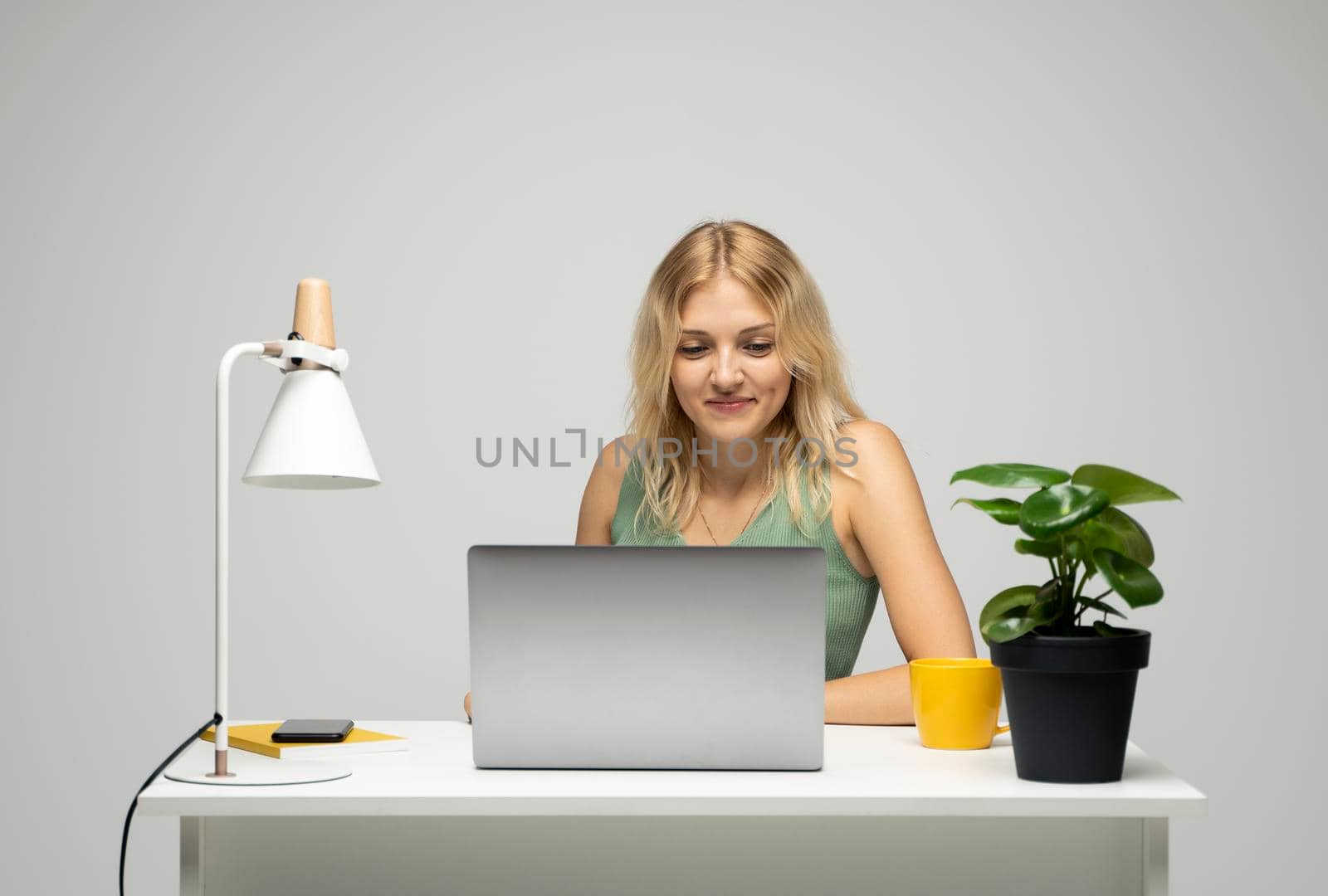 Portrait of a pretty young woman studying while sitting at the table with grey laptop computer, notebook