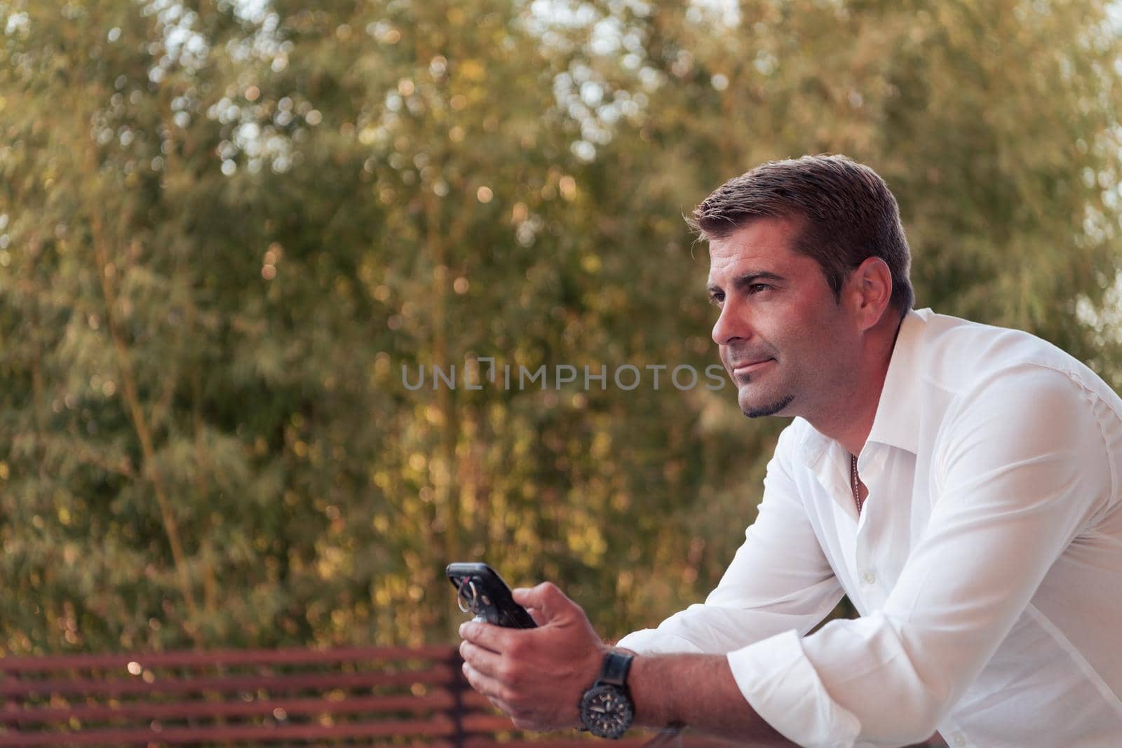 A businessman in casual clothes resting on the balcony of the terrace while using a smartphone. Selective focus by dotshock