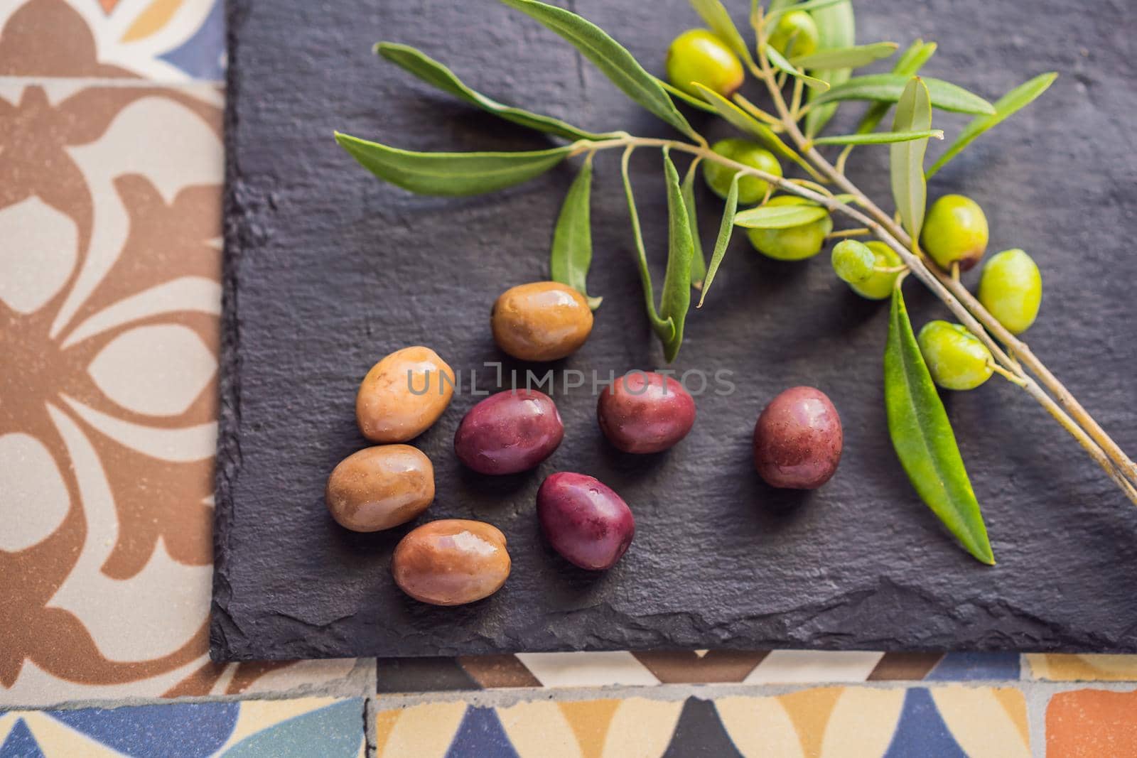 Green and black olives with leaves on dark background. Copy space, flat lay.