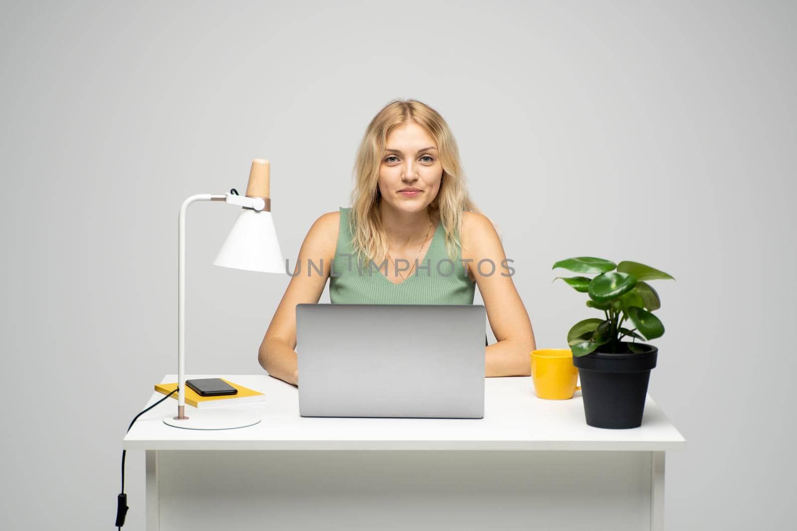 Smiling business woman working with a laptop isolated on a grey background. Portrait of a pretty young woman studying while sitting at the table with grey laptop computer, notebook. by vovsht