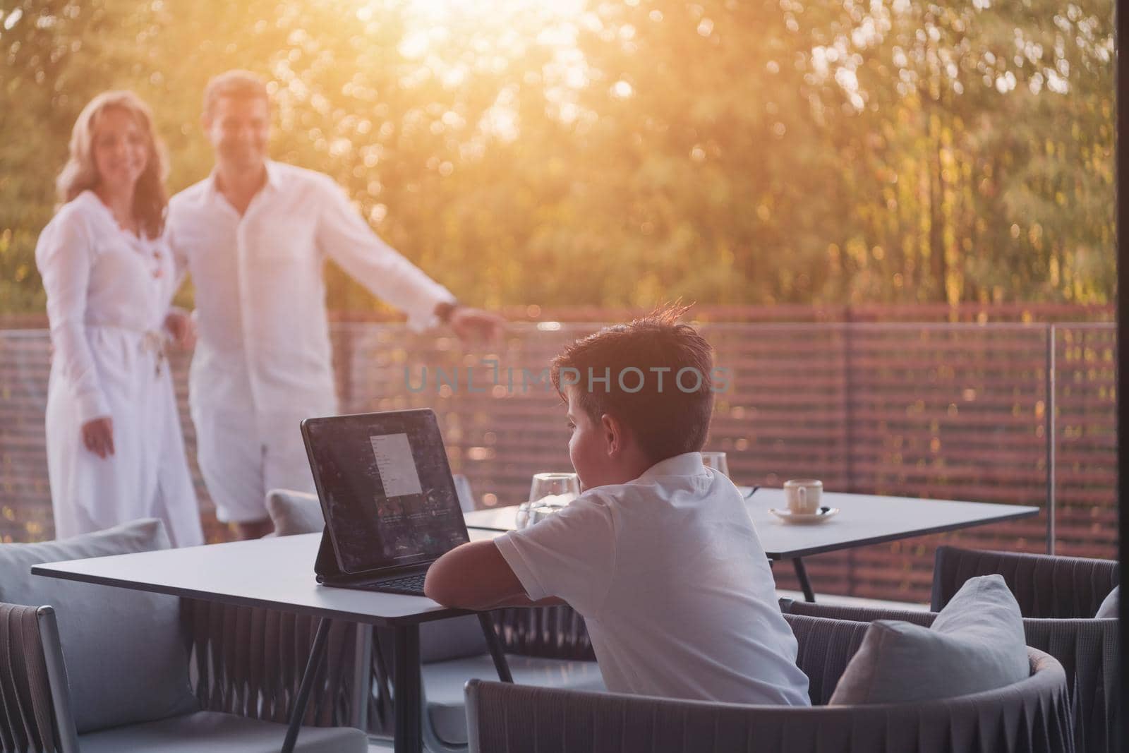 Happy elderly couple resting on the balcony of a luxury house while their son using a tablet. Selective focus. High-quality photo