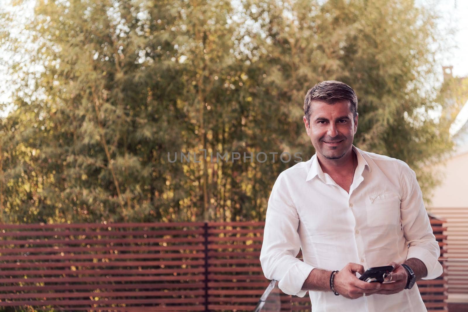 A businessman in casual clothes resting on the balcony of the terrace while using a smartphone. Selective focus. High-quality photo