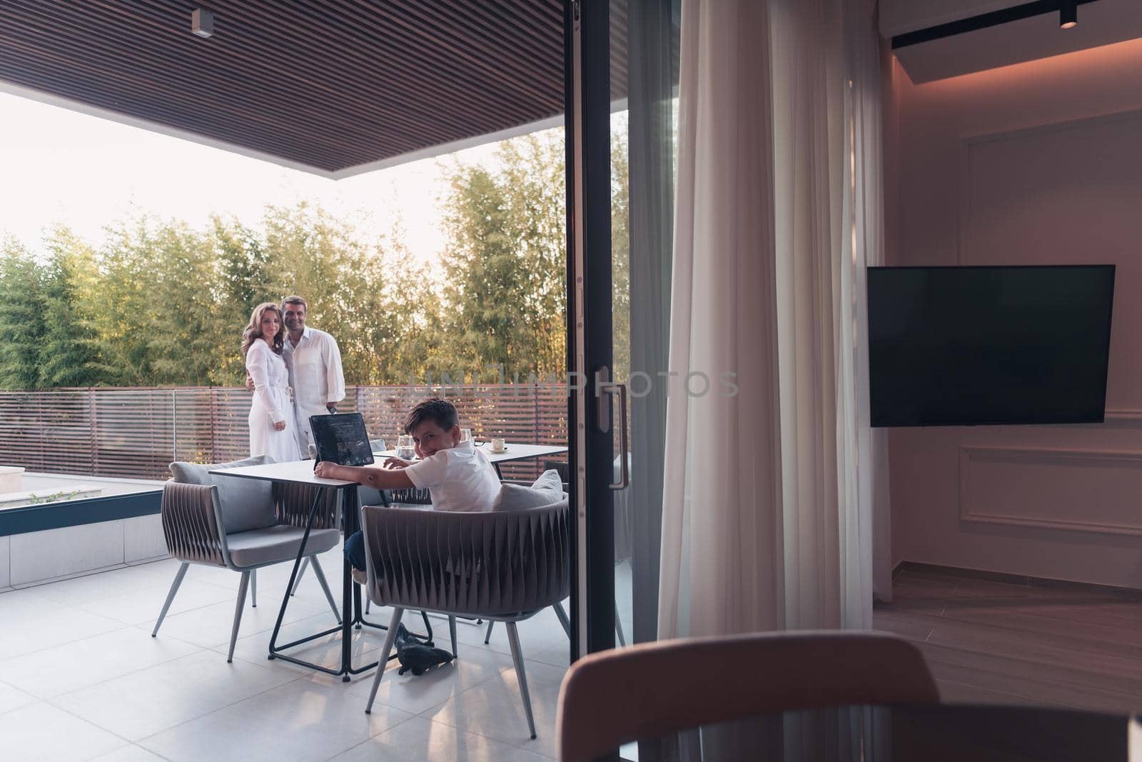 Happy elderly couple resting on the balcony of a luxury house while their son using a tablet. Selective focus by dotshock