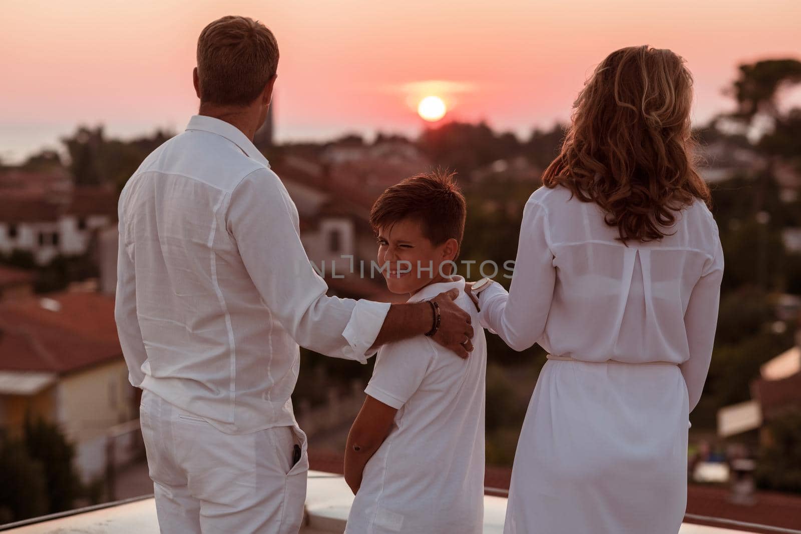 The happy family enjoys and spends time together on the roof of the house while watching the sunset on the open sea together. High-quality photo