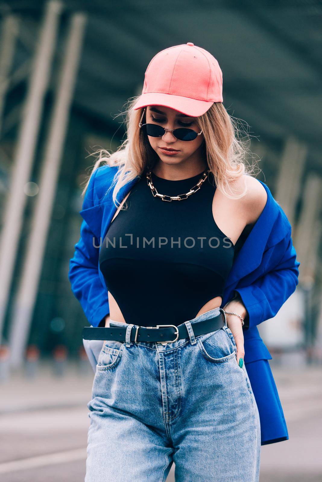 Young sexy blonde hipster woman posing on the street. Wearing blue stylish jacket, jeans and baseball hat and sunglasses. by Ashtray25