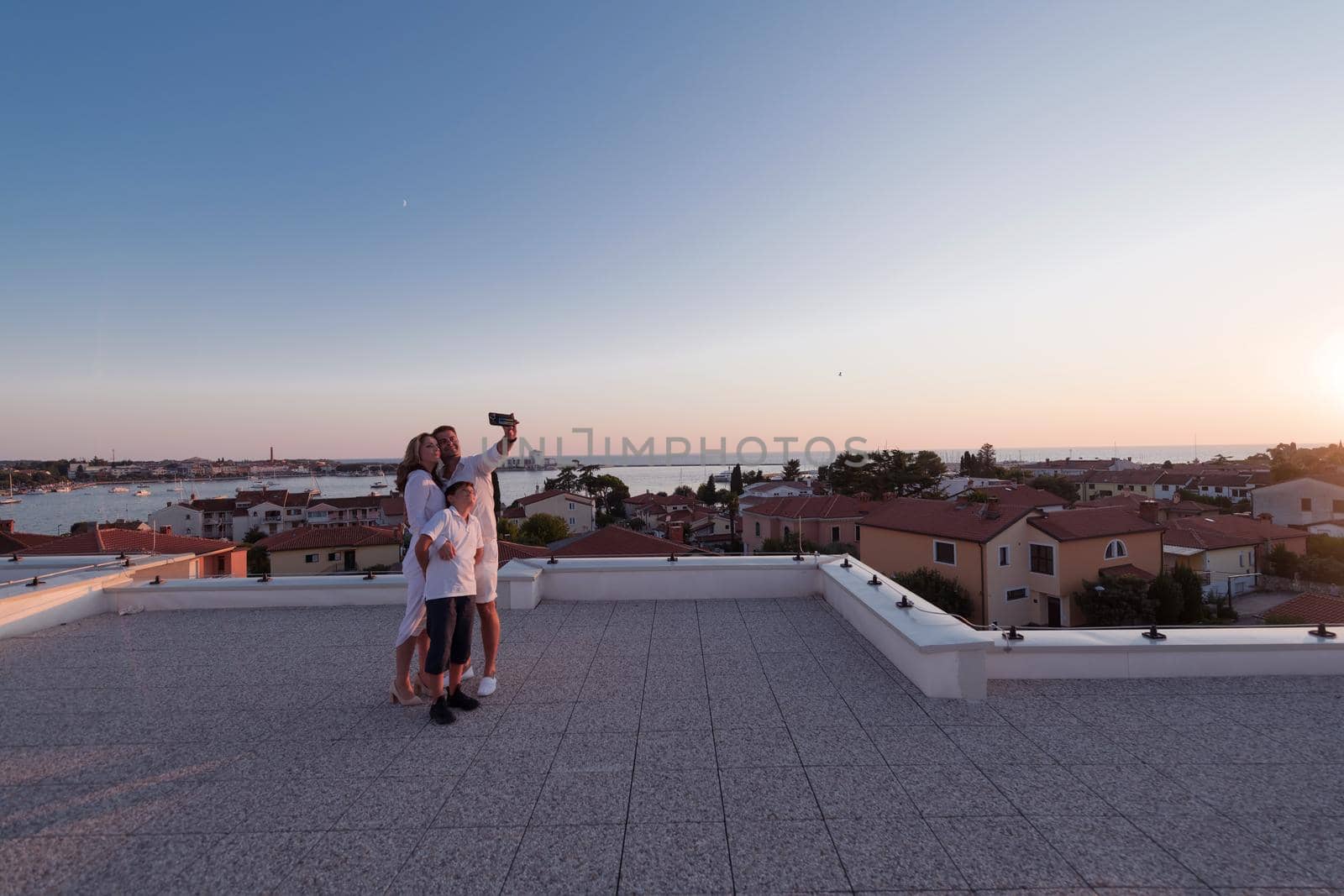 Happy family taking a selfie with a smartphone on the roof of their house at sunset. Selective focus by dotshock