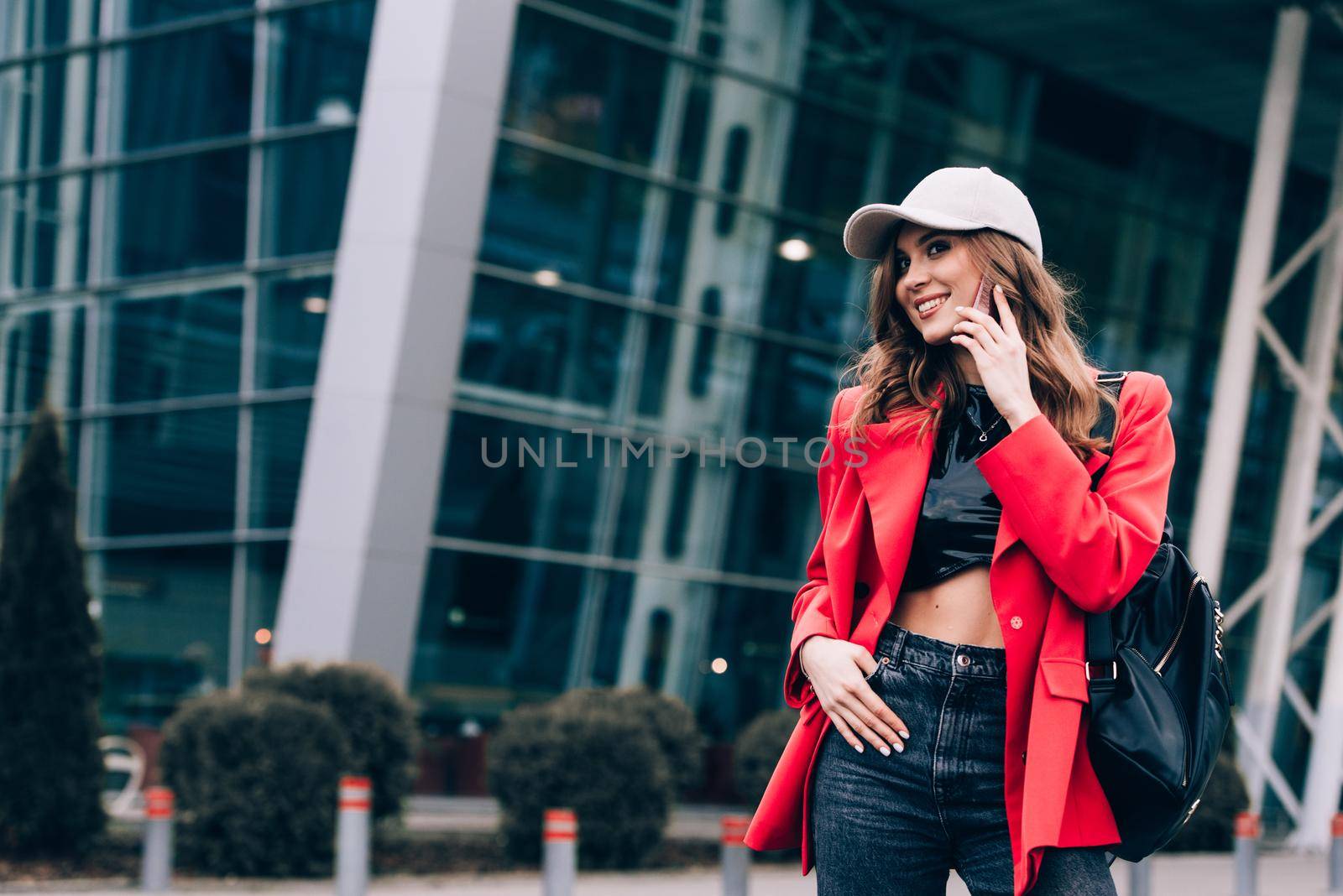 Stylish woman on the street uses a mobile phone. beautiful woman with long dark hair in a red jacket, black top and a cap