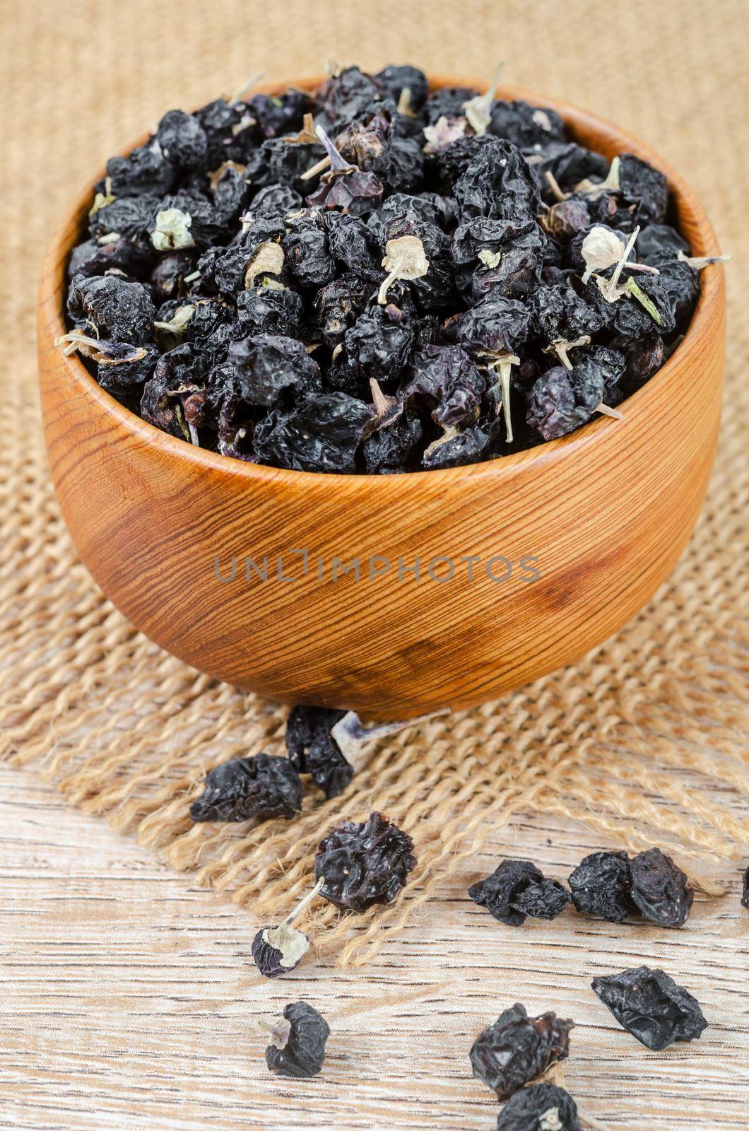 Black wolfberries or black goji berries, in a wooden bowl on table.