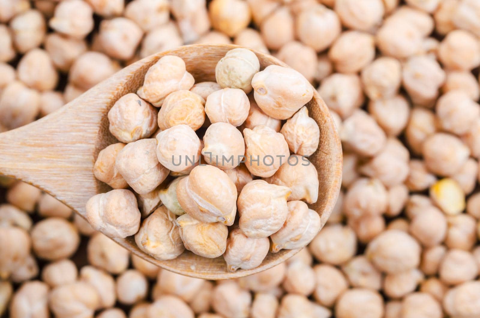 The uncooked chickpeas on wooden scoop.