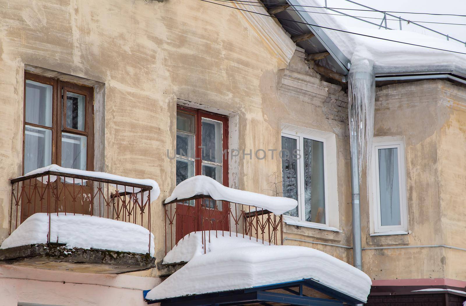 Sharp ice icicles hang from the drainpipe at the edge of the roof. Against the background of the wall of an old brick house. Large cascades, even beautiful rows. Cloudy winter day, soft light.