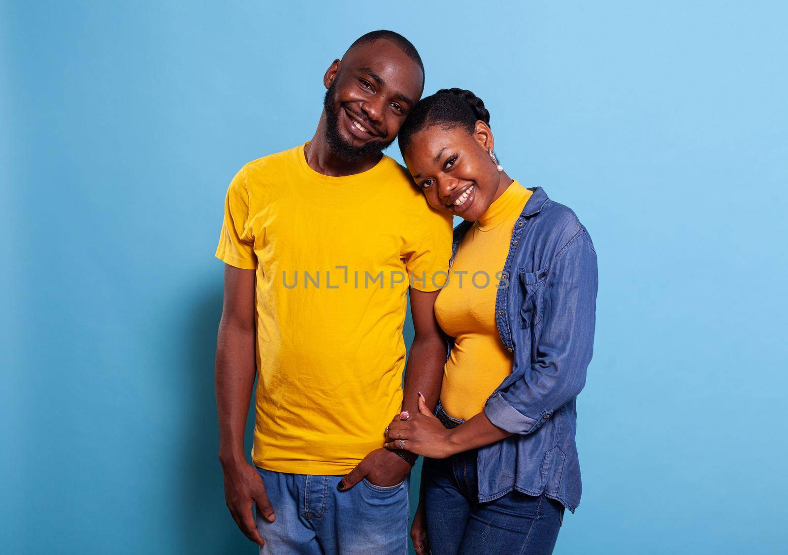 Portrait of young couple holding hands over blue background, showing love and gratitute for each other. Girlfriend and boyfriend expressing fondness and smiling, feeling happy in relationship.