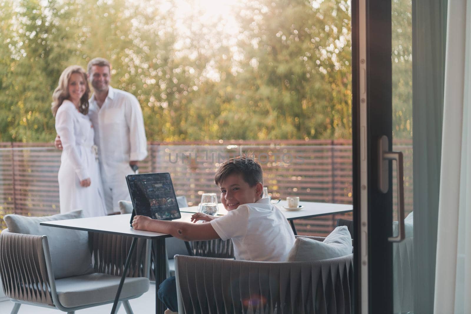 Happy elderly couple resting on the balcony of a luxury house while their son using a tablet. Selective focus. High-quality photo