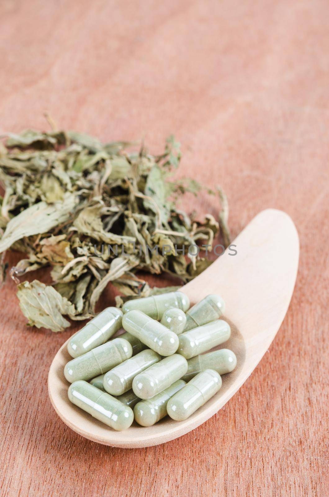 Pile of herbal medicine in capsules with herb dry leaf on wooden background.
