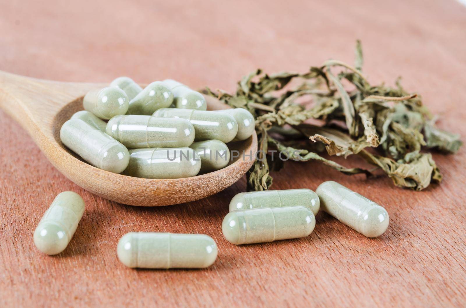 Pile of herbal medicine in capsules with herb dry leaf on wooden background.