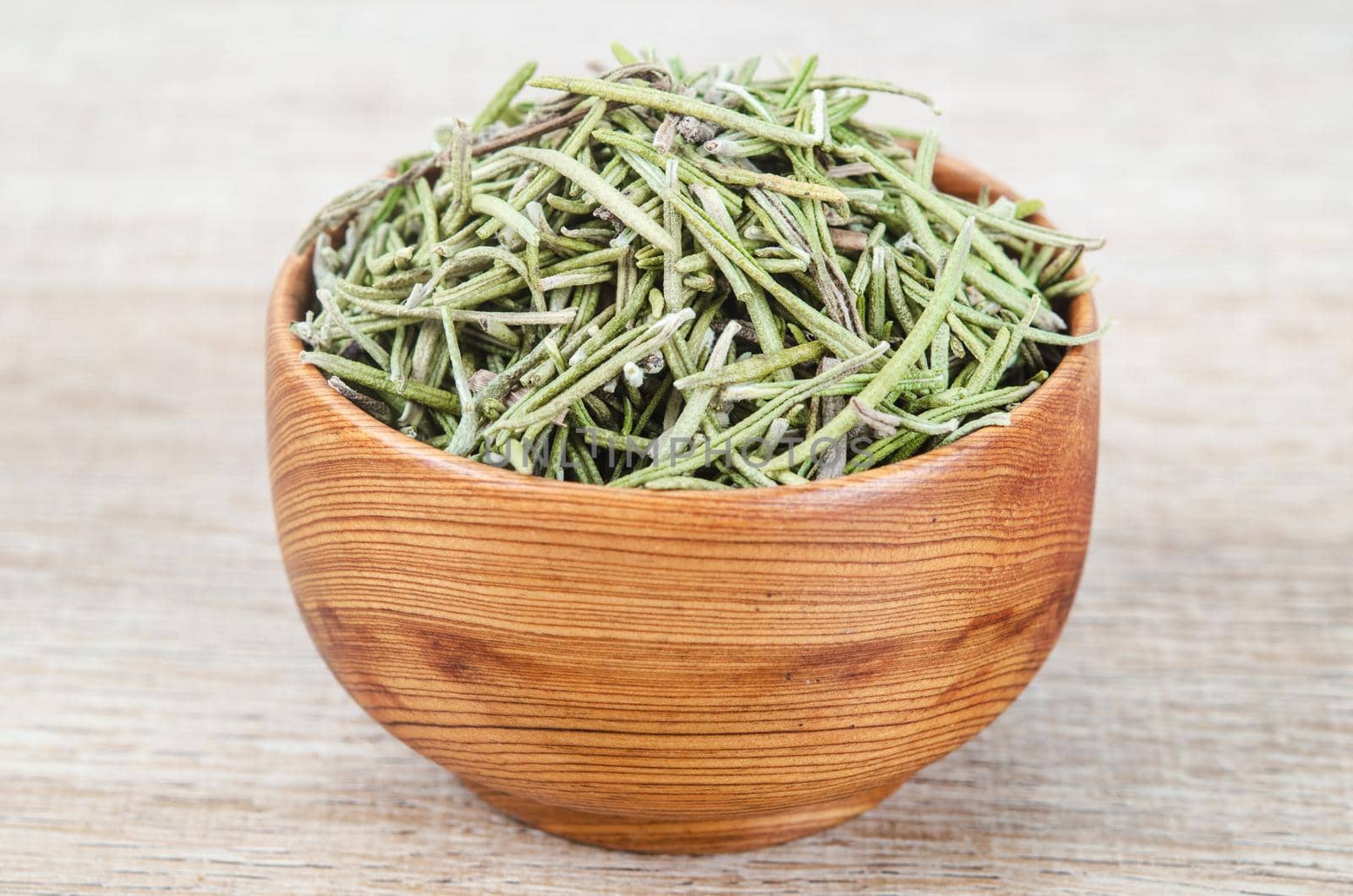Dried rosemary spice in wooden bowl. Macro with shallow depth of field.