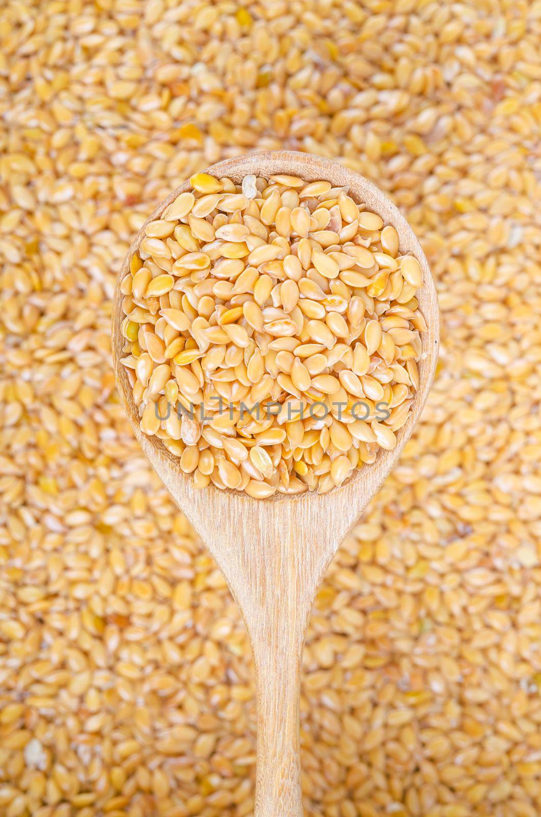 The Gold flax seeds in a wooden spoon on a flax seeds background.