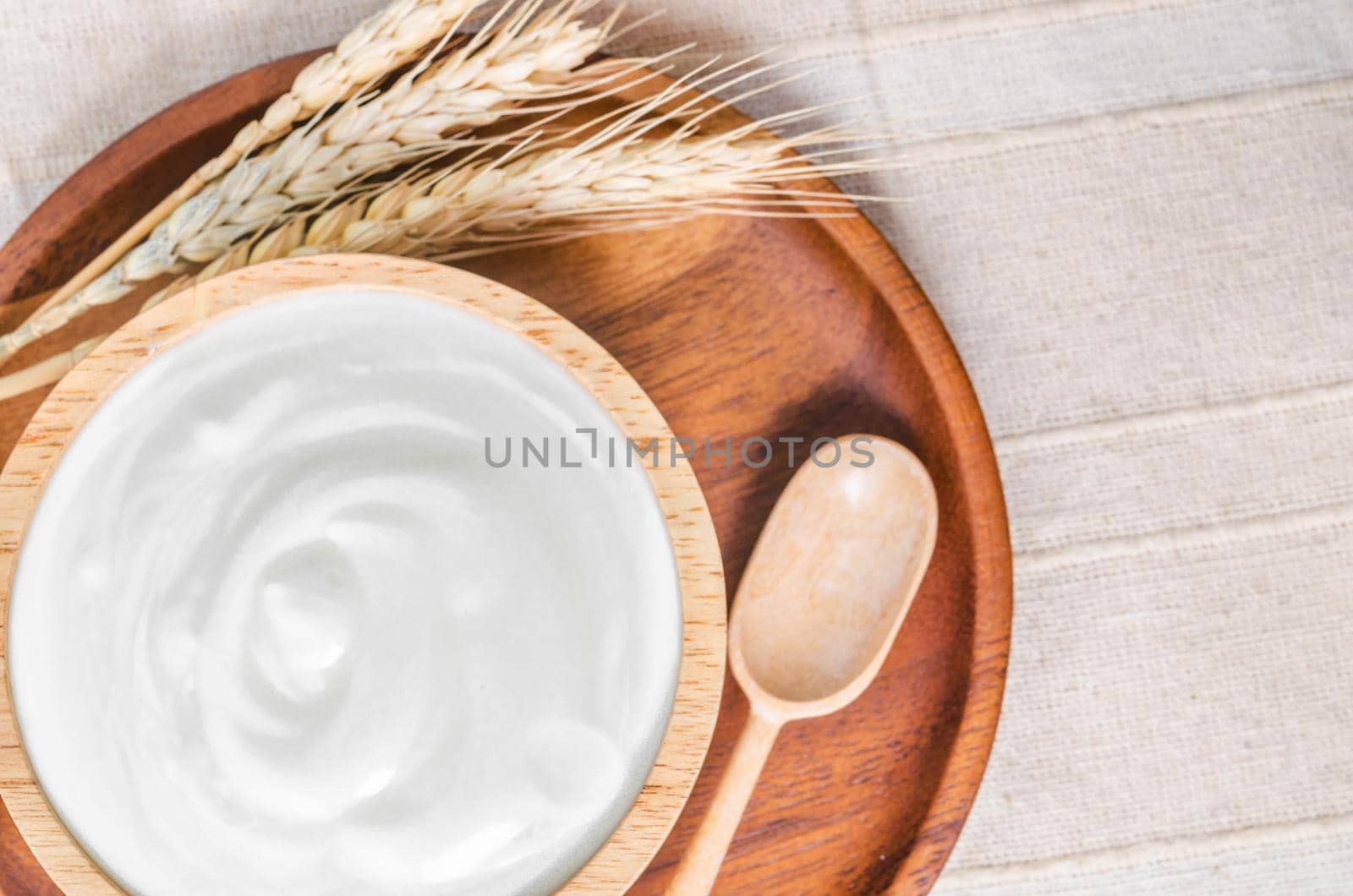 The Greek yogurt in a wooden bowl and dry barley on tablecloth.