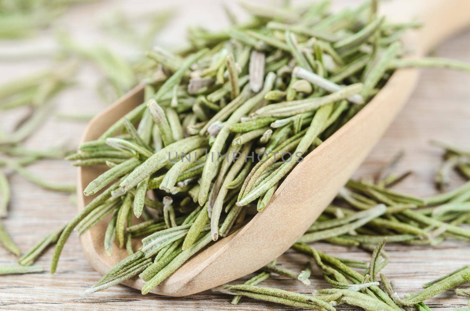 Dried rosemary spice in wooden spoon. Macro with shallow depth of field.