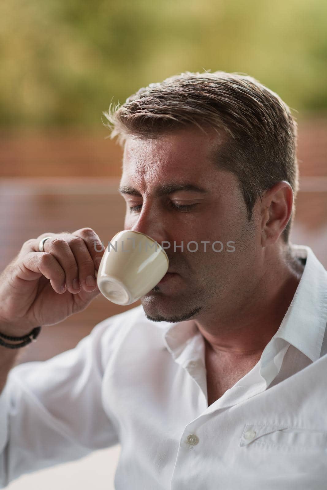 A senior businessman in casual clothes sits on the terrace of a luxury house and drinks morning coffee. Selective focus. High-quality photo