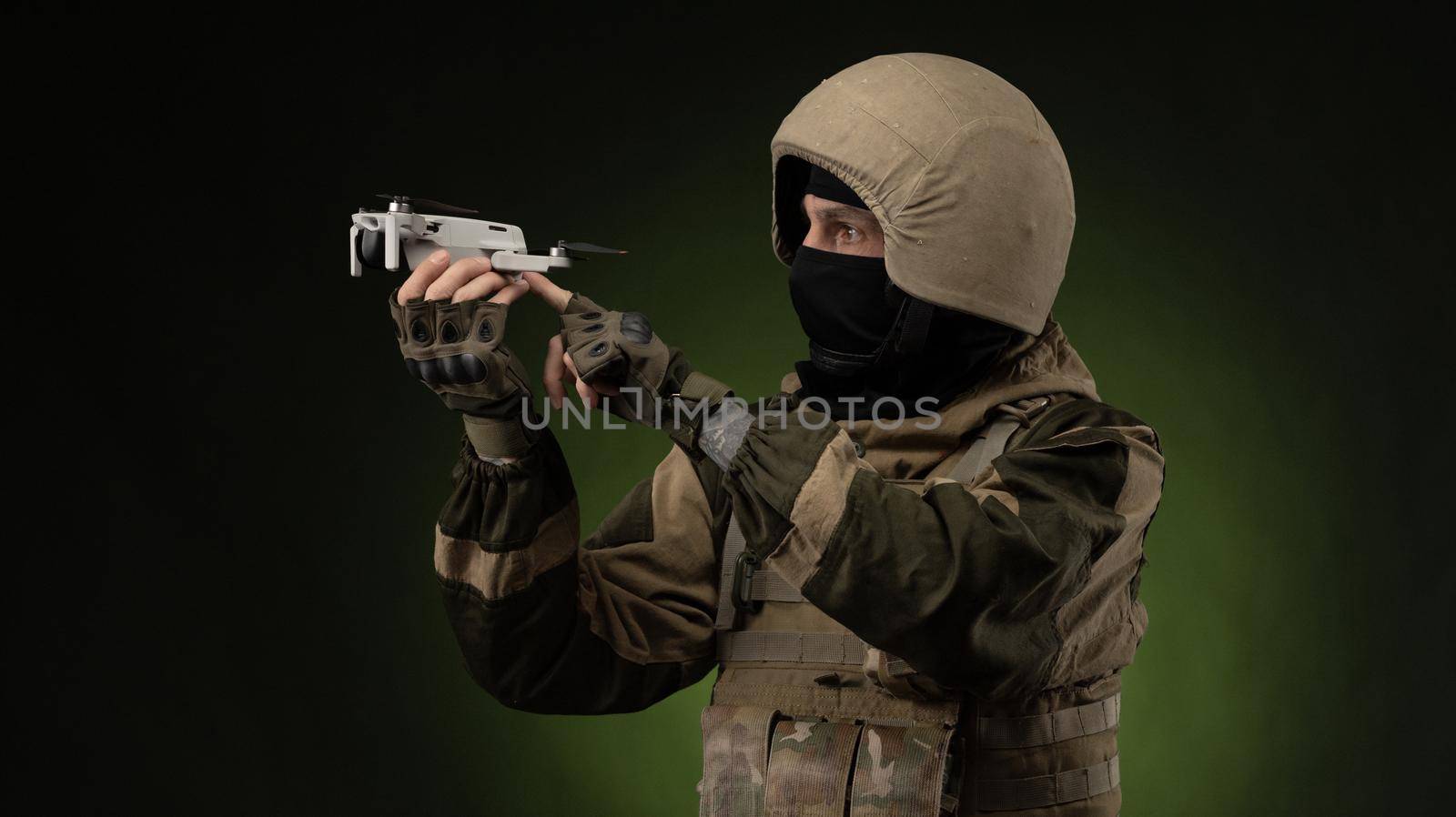 a soldier in military clothes with a weapon launches a small unmanned quadcopter for reconnaissance on a dark background by Rotozey