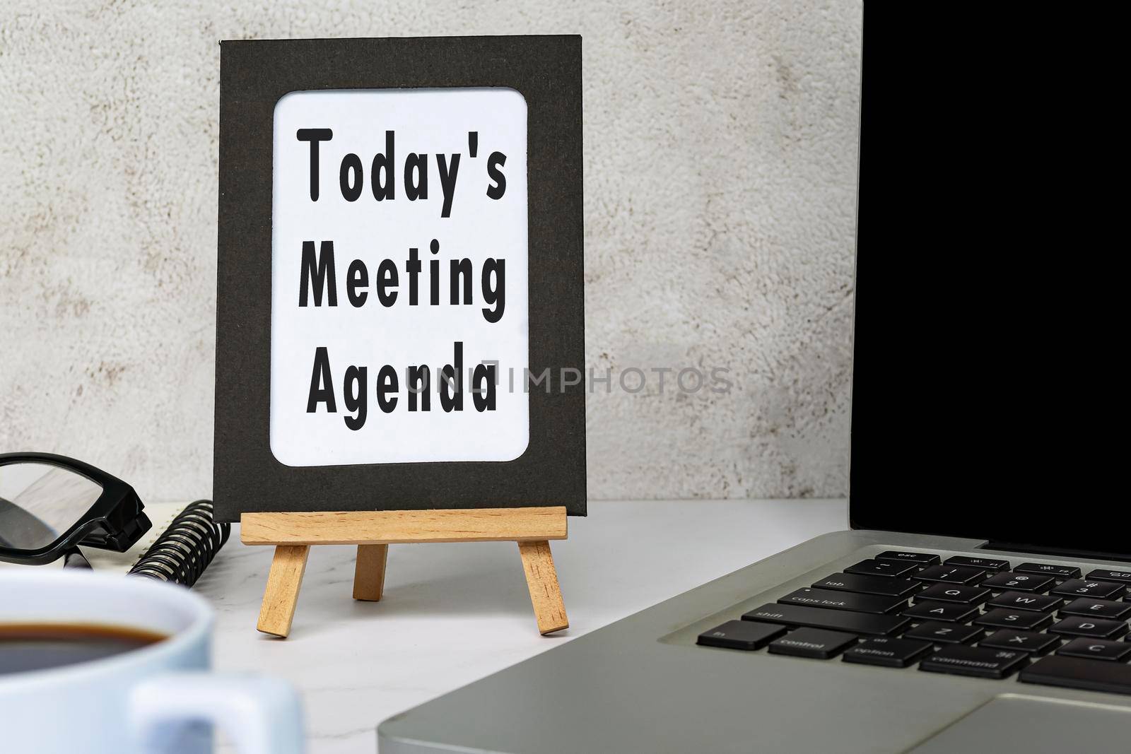 Today's meeting agenda text written on chalkboard with notebook on white desk. Meeting and goal concept.