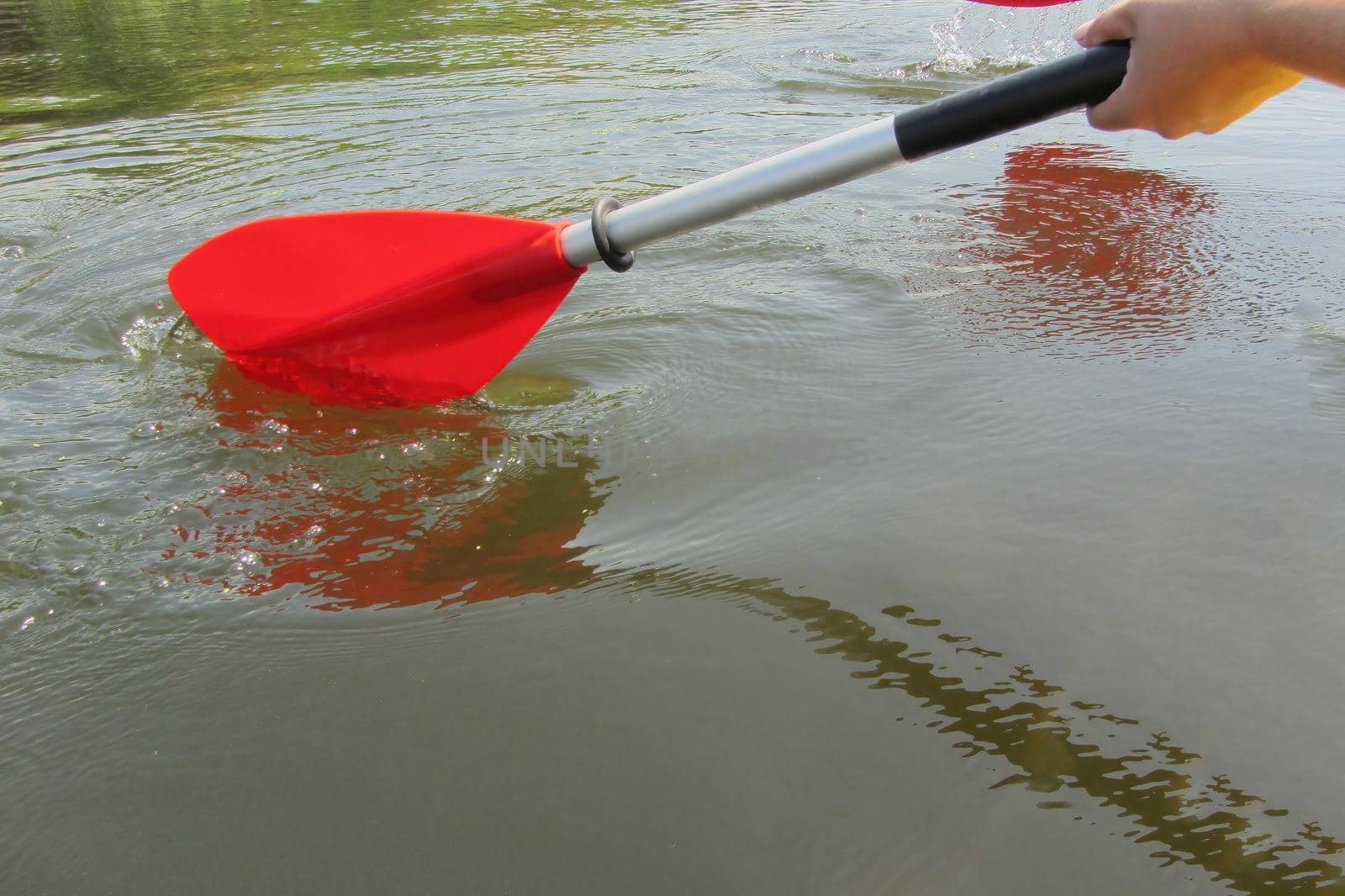 On image: Red paddles for white water rafting and kayaking. Close up of a hand with red paddle kayaking or rafting on the river, concept of spring water sports. Selective focus.