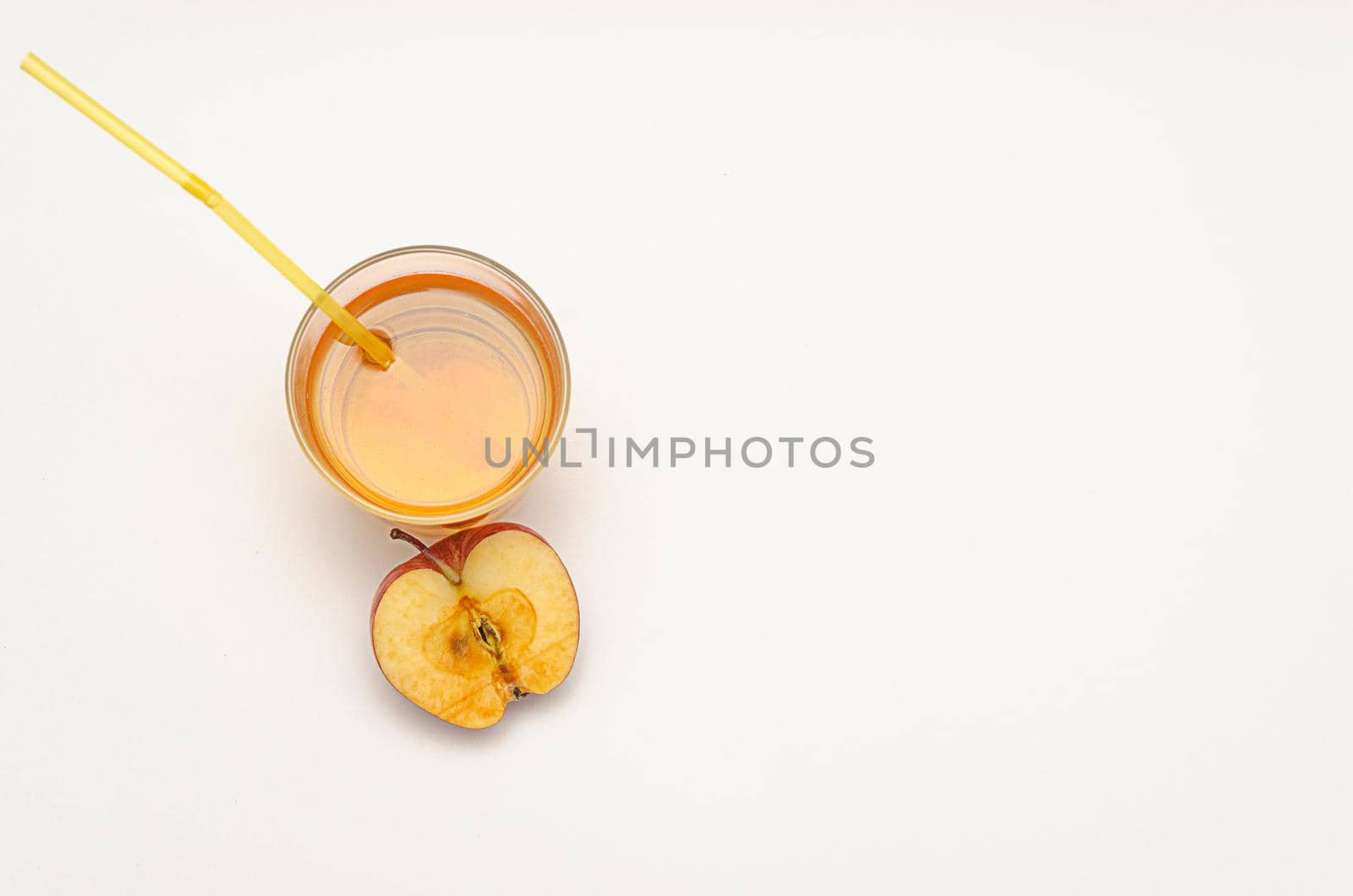 a glass of apple juice with a straw and half a red apple on a white background, copy space