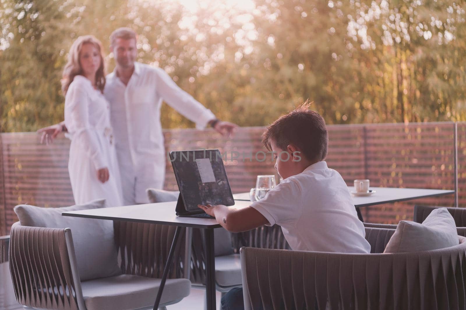 Happy elderly couple resting on the balcony of a luxury house while their son using a tablet. Selective focus by dotshock