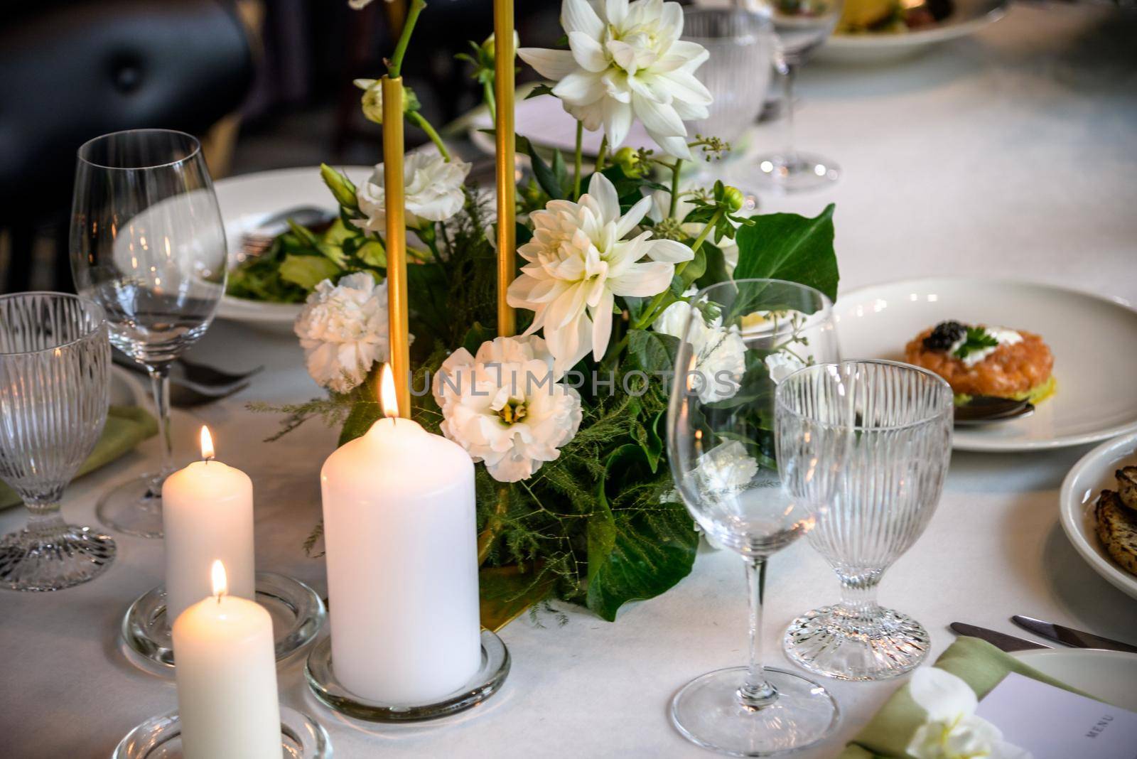 Wedding banquet. The festive table is served with plates with napkins and name cards, glasses and cutlery, and decorated with flower arrangements and candles.