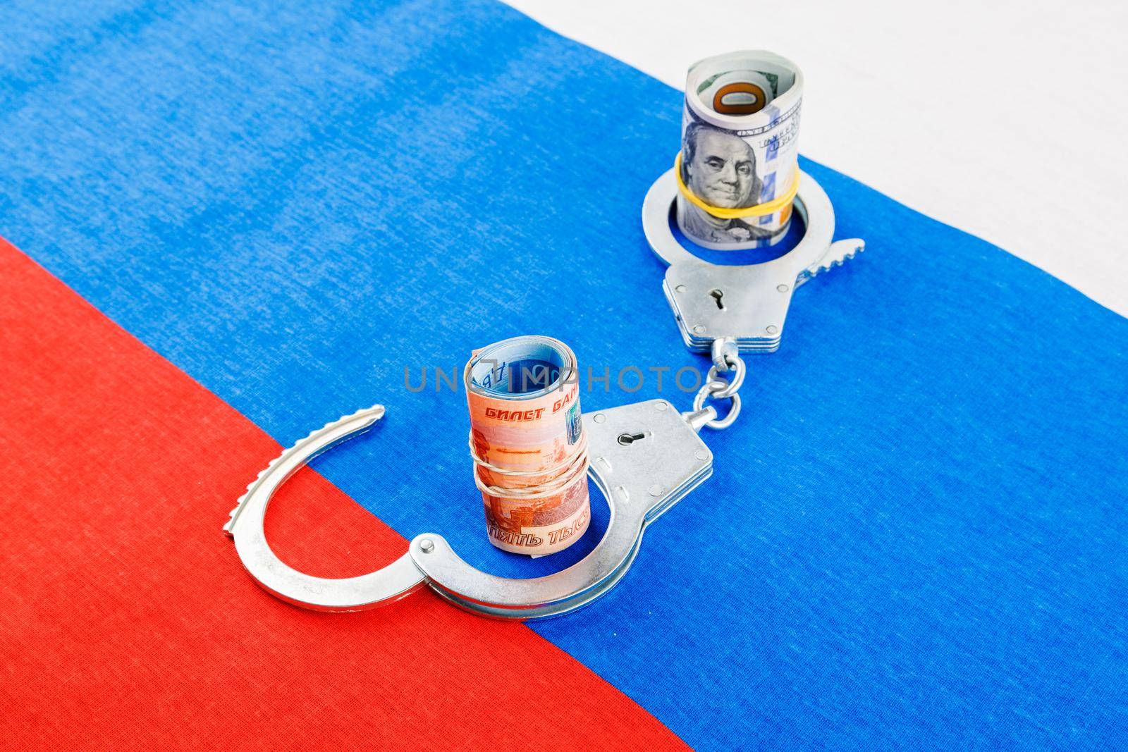 roll of us dollar banknotes in a handcuffs with a roll of russian ruble banknotes on flat full-frame russian flag background, closeup