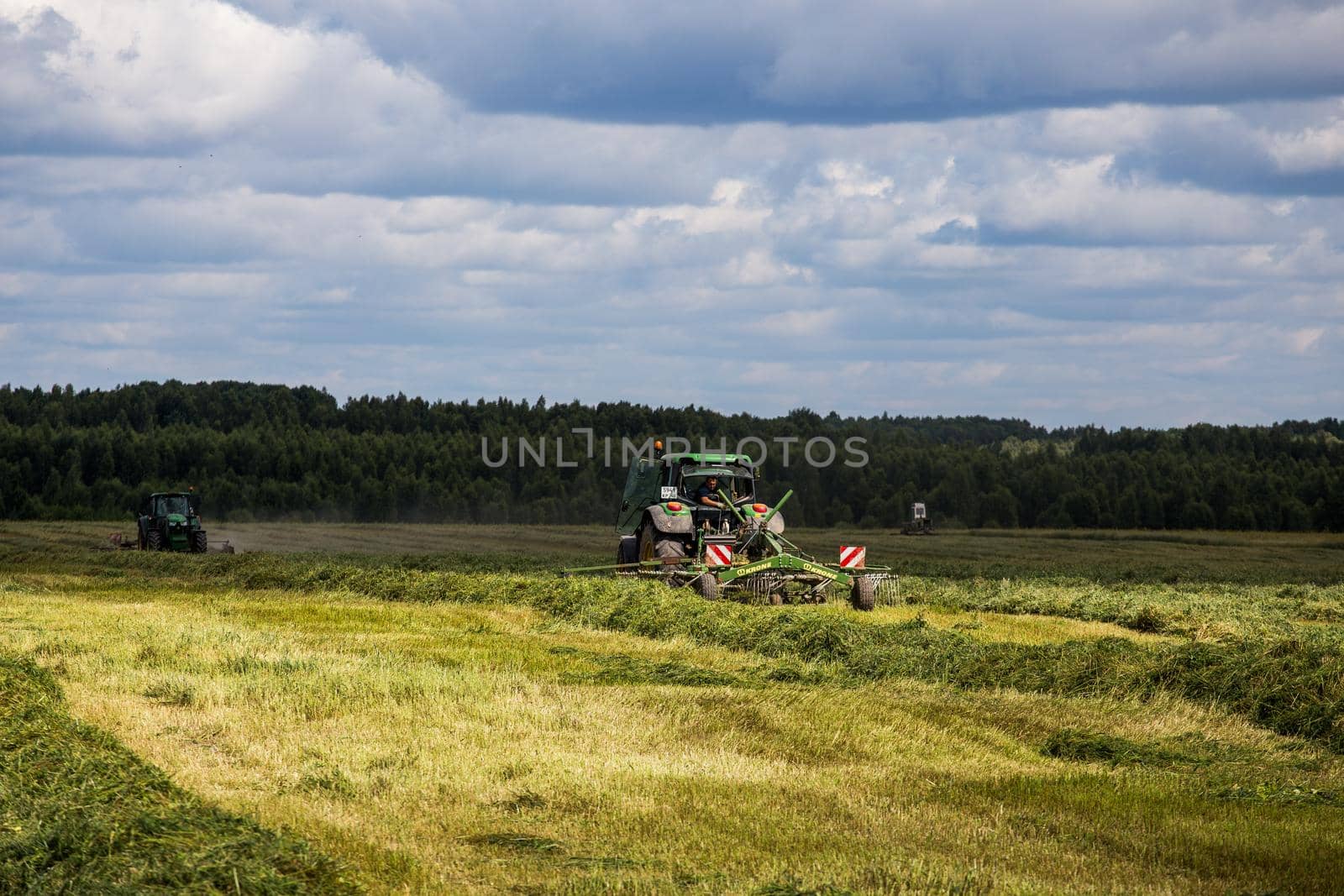 two green haymaking John Deere tractors with Krone plow on summer field before storm - telephoto shot with selective focus by z1b