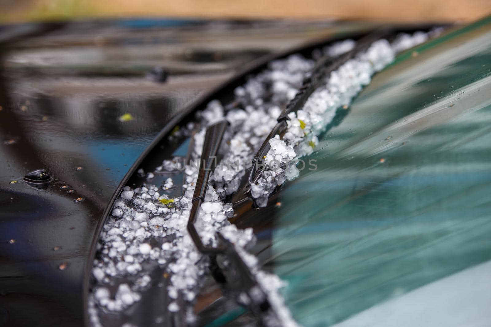 small hail ice balls on black car hood after heavy summer storm close-up with selective focus at daylight.