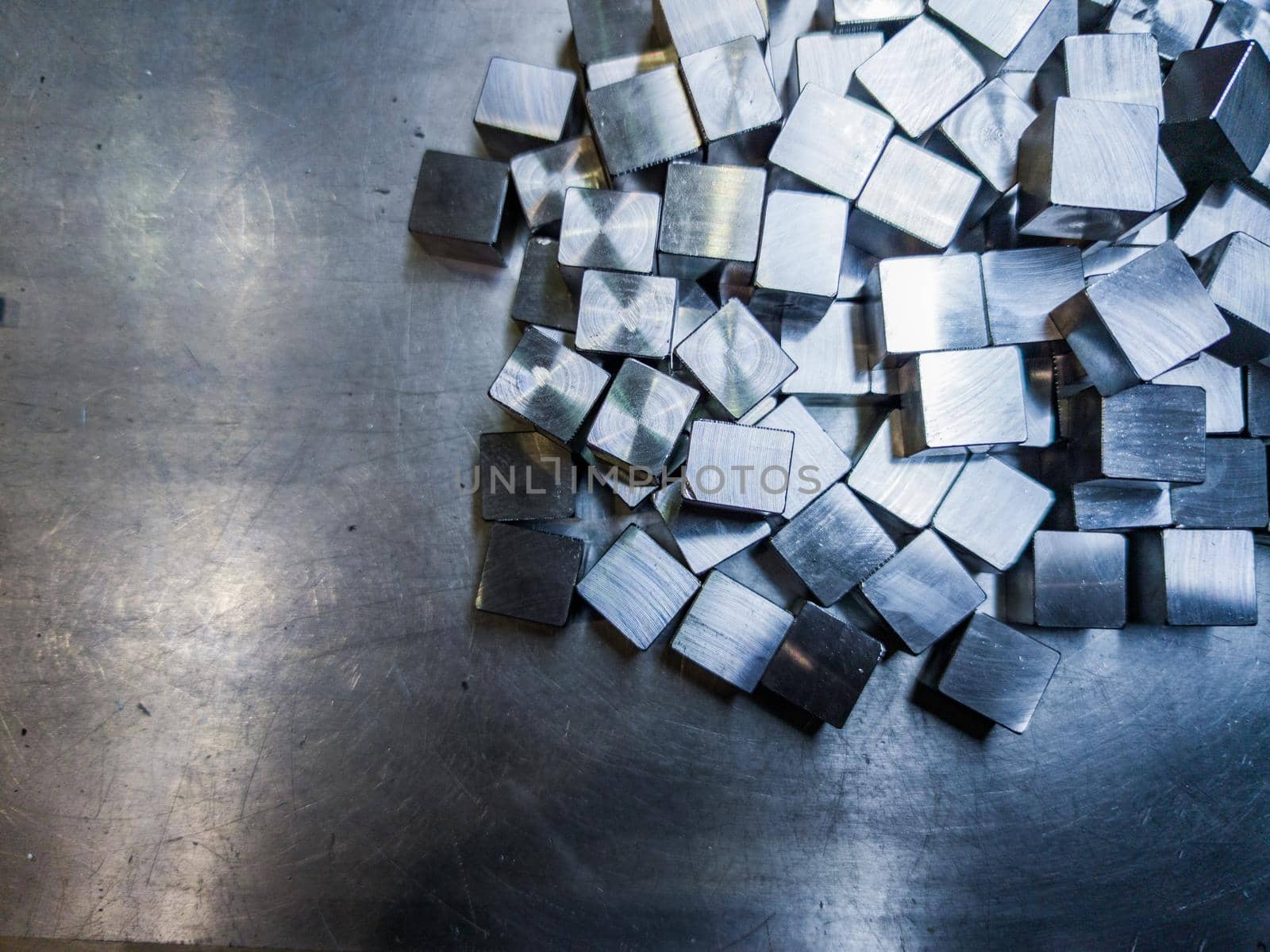 pile of small machined shiny steel cubes on metal surface, closeup with selective focus