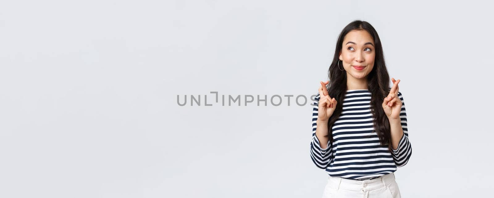 Lifestyle, people emotions and casual concept. Hopeful cute wishful asian girl cross fingers good luck, looking up at lottery and making wish, dreaming of something, white background.