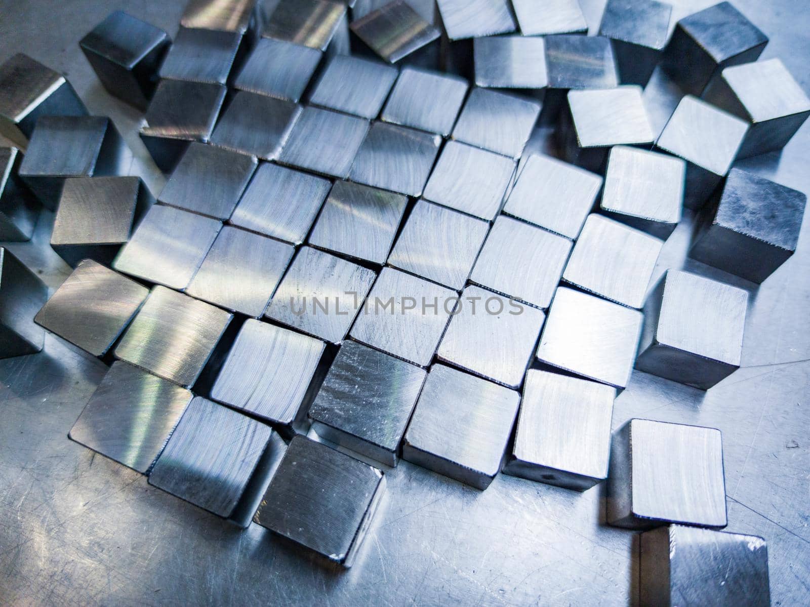 pile of small machined shiny steel cubes on metal surface, closeup with selective focus