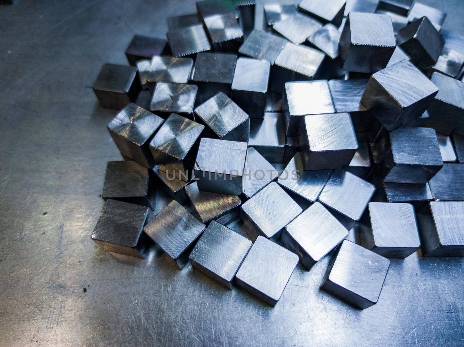 pile of small machined shiny steel cubes on metal surface, closeup with selective focus