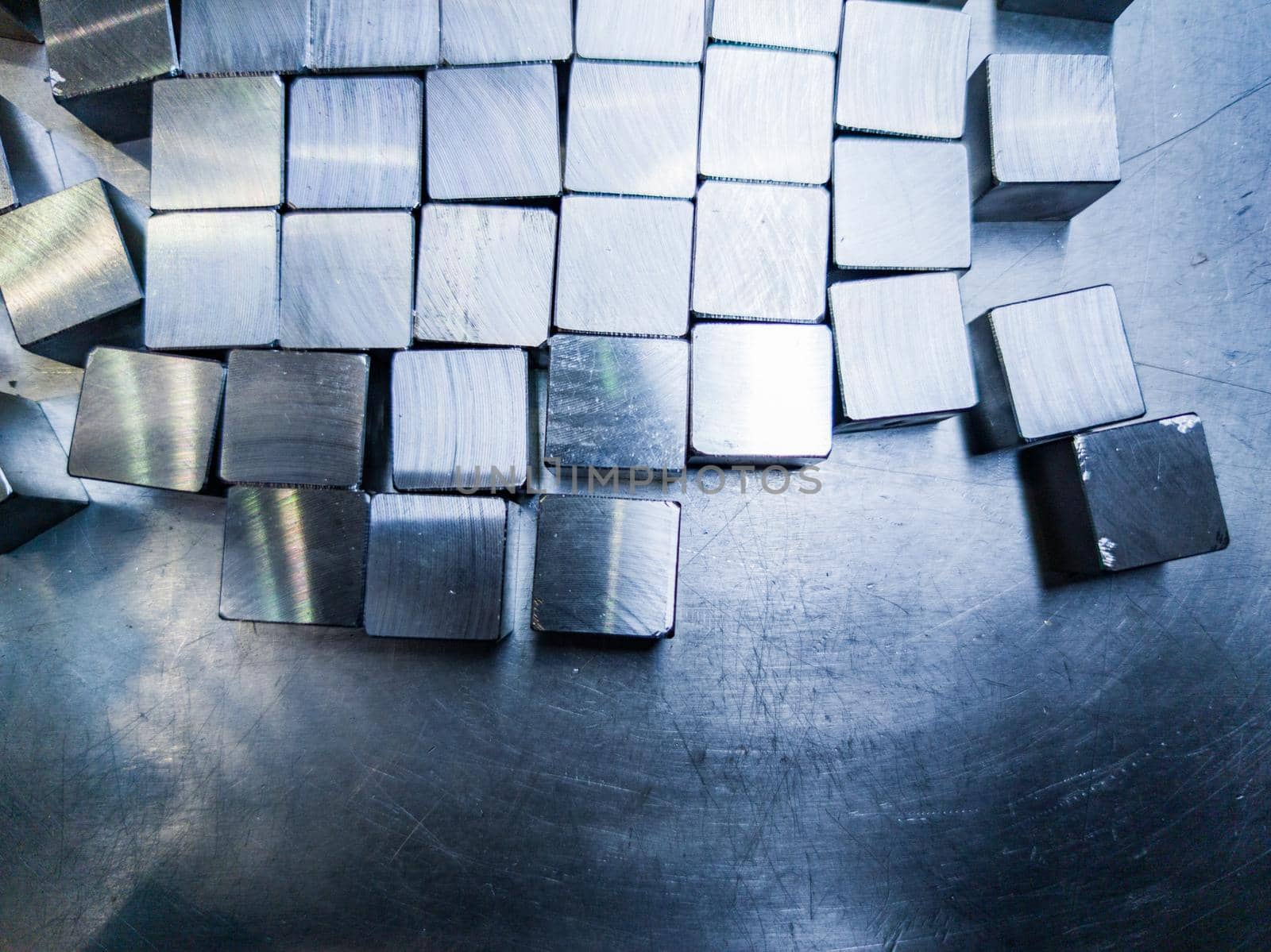 pile of small machined shiny steel cubes on metal surface, closeup with selective focus