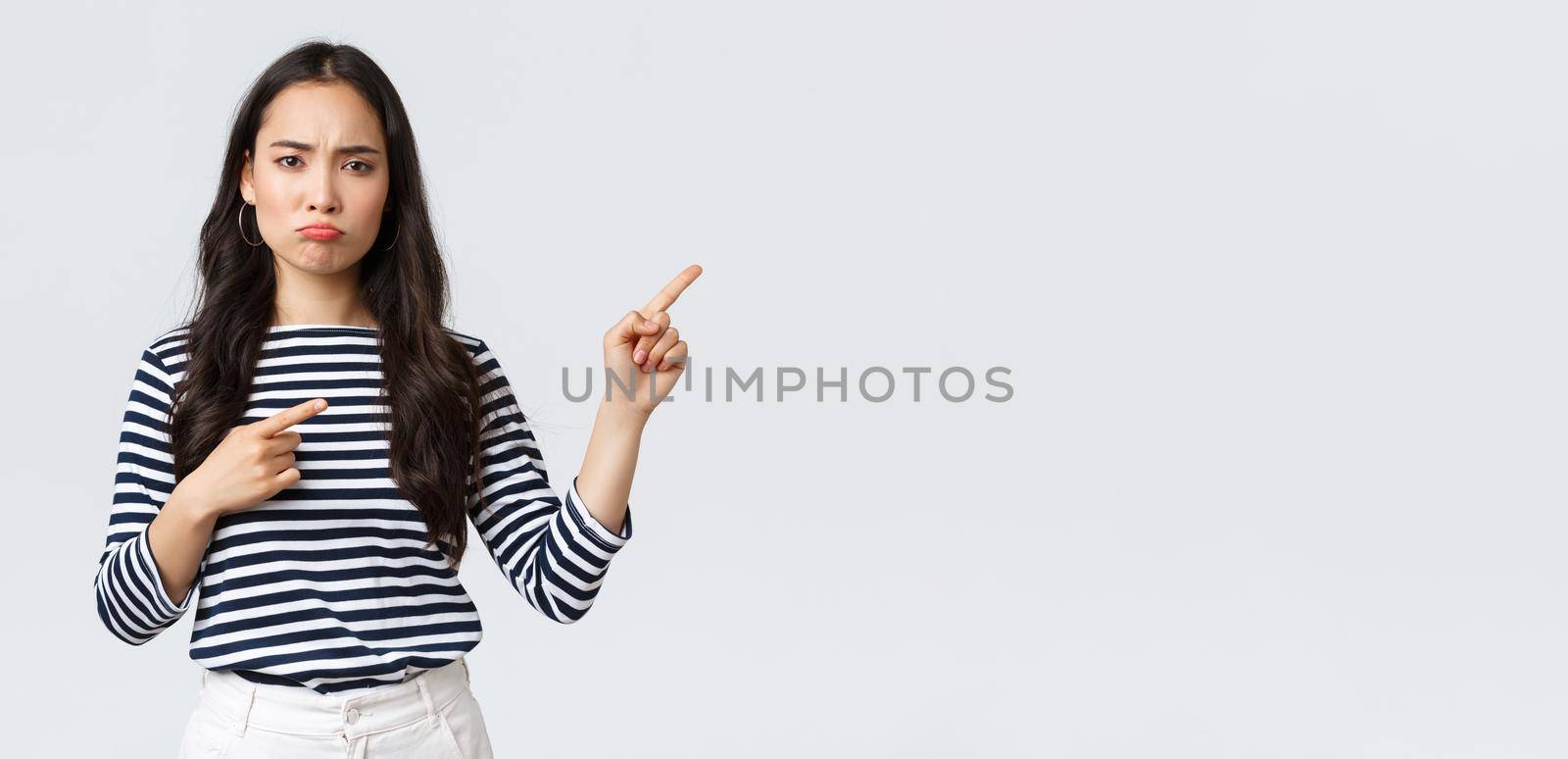 Lifestyle, beauty and fashion, people emotions concept. Disappointed upset young asian woman pouting and frowning displeased, pointing fingers right top as complaining about product or service by Benzoix