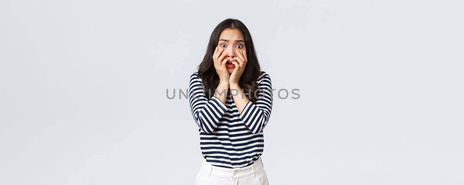 Lifestyle, people emotions and casual concept. Scared timid and insecure woman hold hands near mouth, screaming and looking terrified, shivering from fear, stand white background by Benzoix