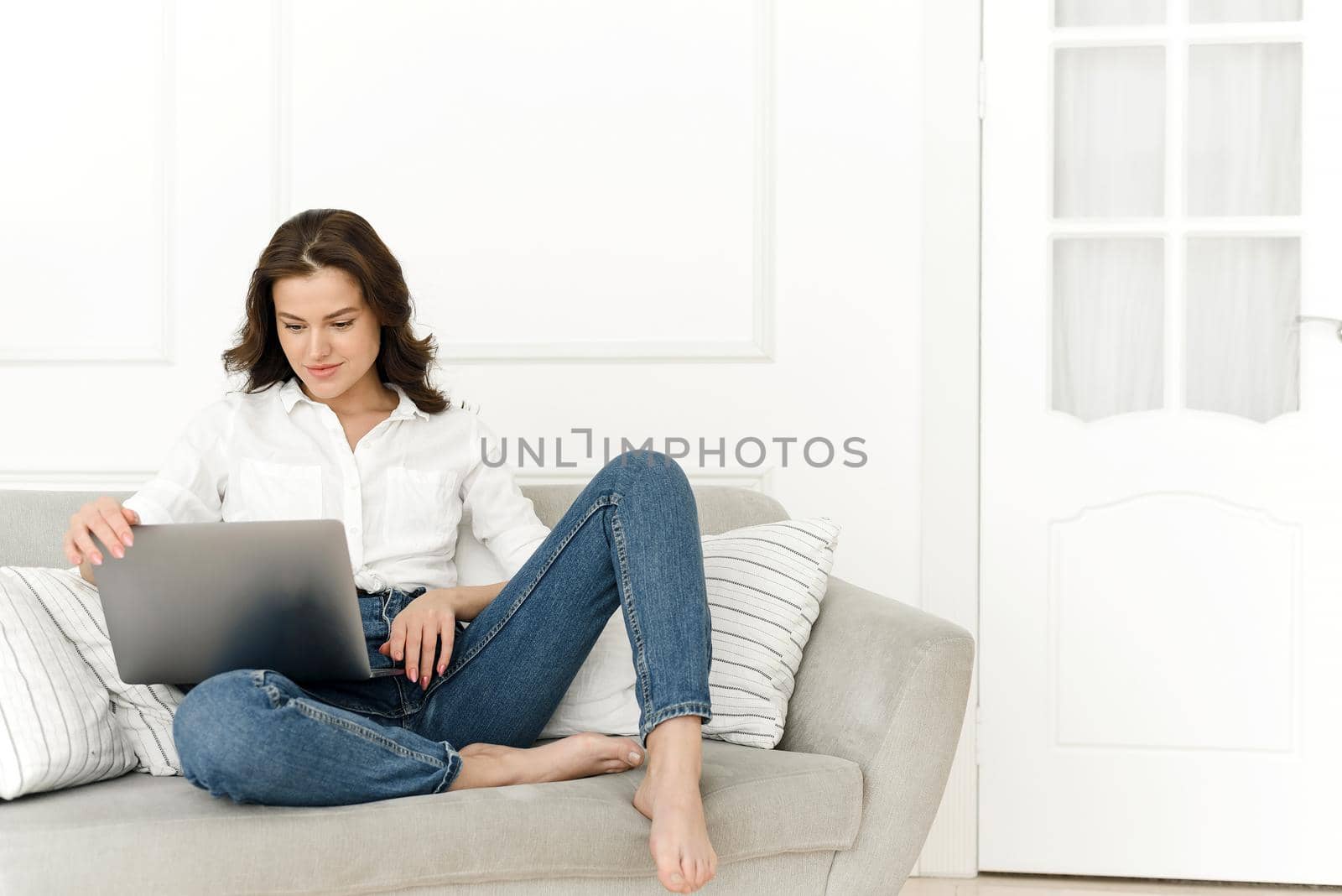 Young positive woman using laptop, checking news on internet, sitting on sofa, working remotely.