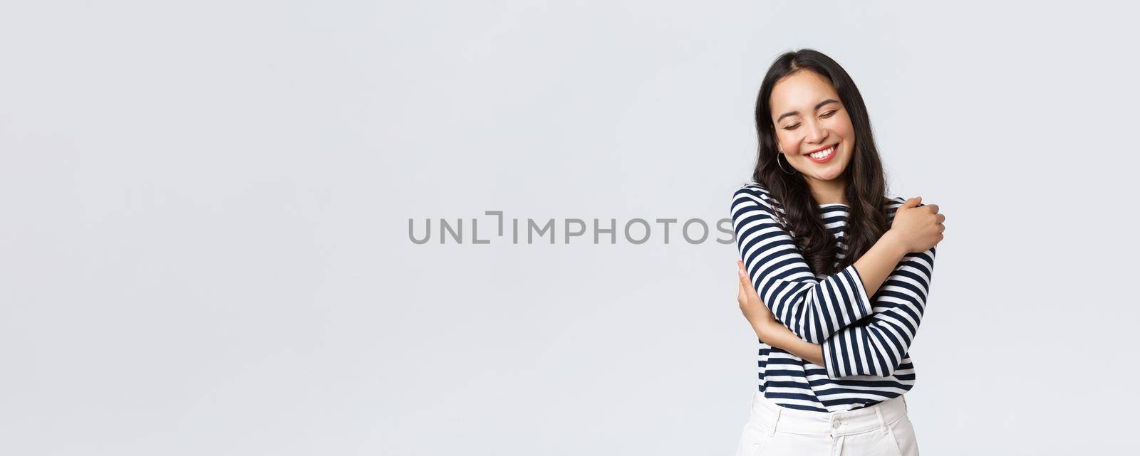 Lifestyle, people emotions and casual concept. Carefree smiling asian bodypositive girl close eyes and laughing carefree, embracing own body, love herself, white background.