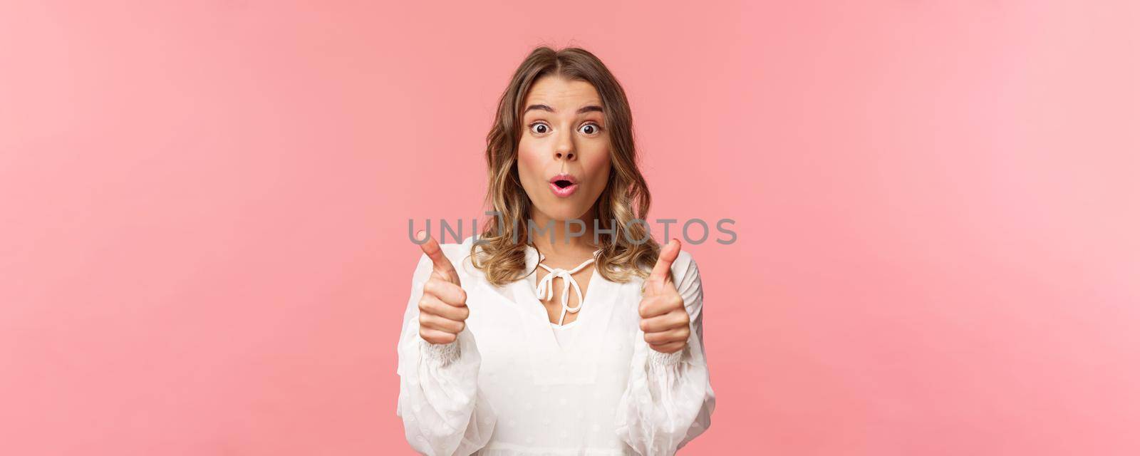 Close-up portrait of impressed blond girl showing thumbs-up look astonished and disbelief as processing fascinating performance she saw, leave positive review, standing pink background.