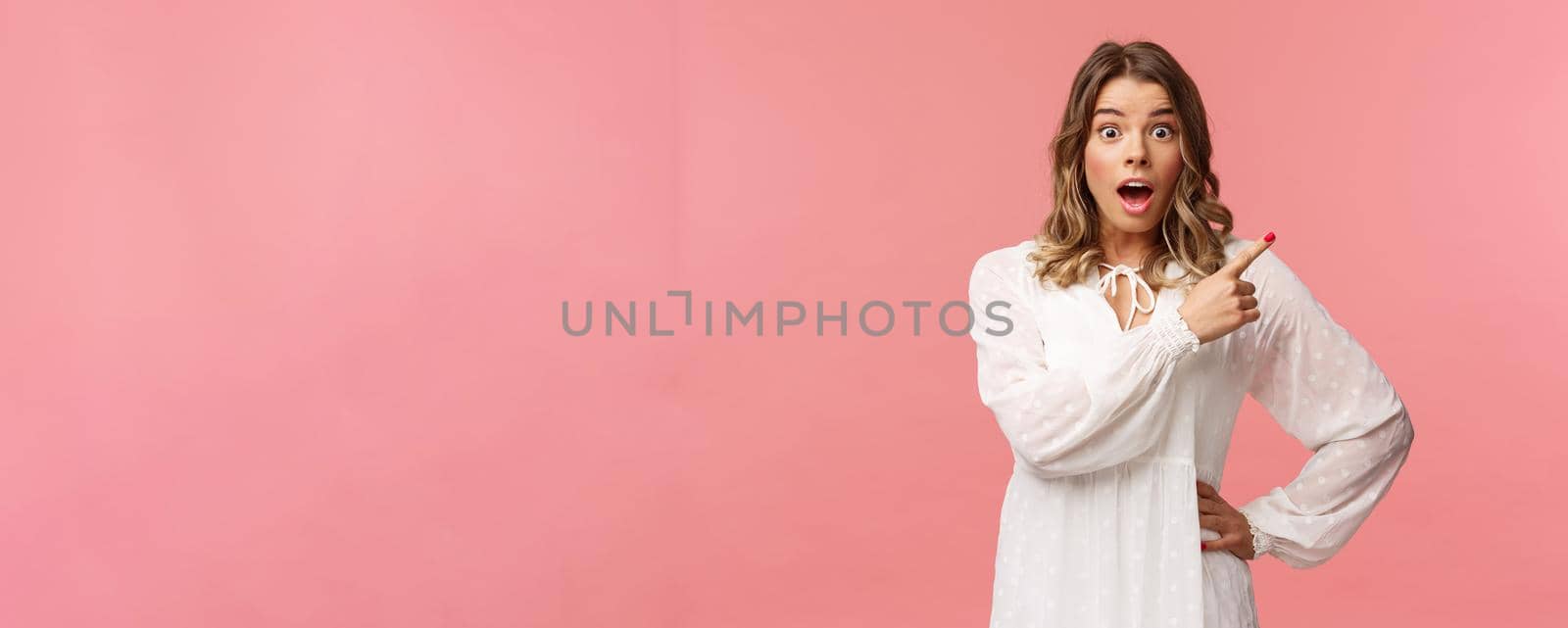 Surprised beautiful blond girl pointing upper right corner, gasping amused and staring at camera with fascinated expression, open mouth in awe to ask question about promo, pink background by Benzoix