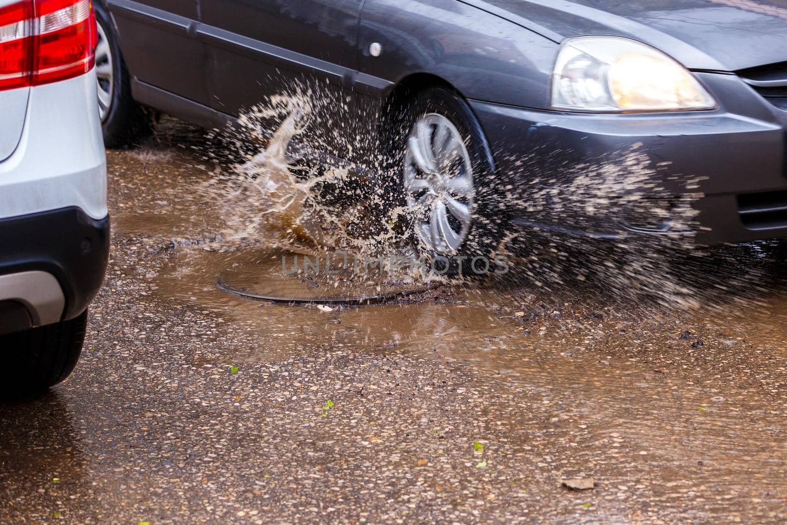 water splashes from car wheel passing summer puddle around manhole cover, close-up with selective focus